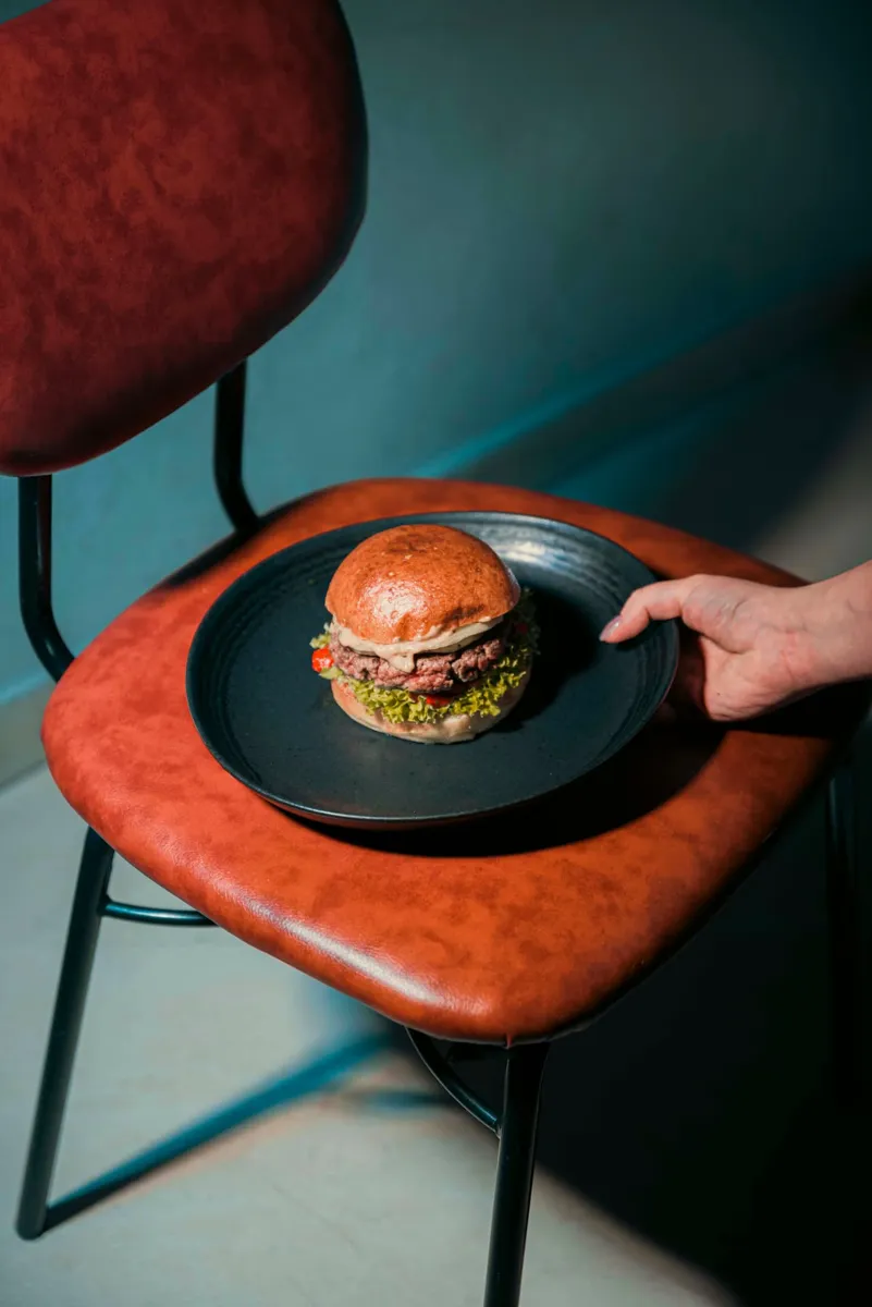 Burger To Beer servito su piatto scuro appoggiato su una sedia in similpelle
