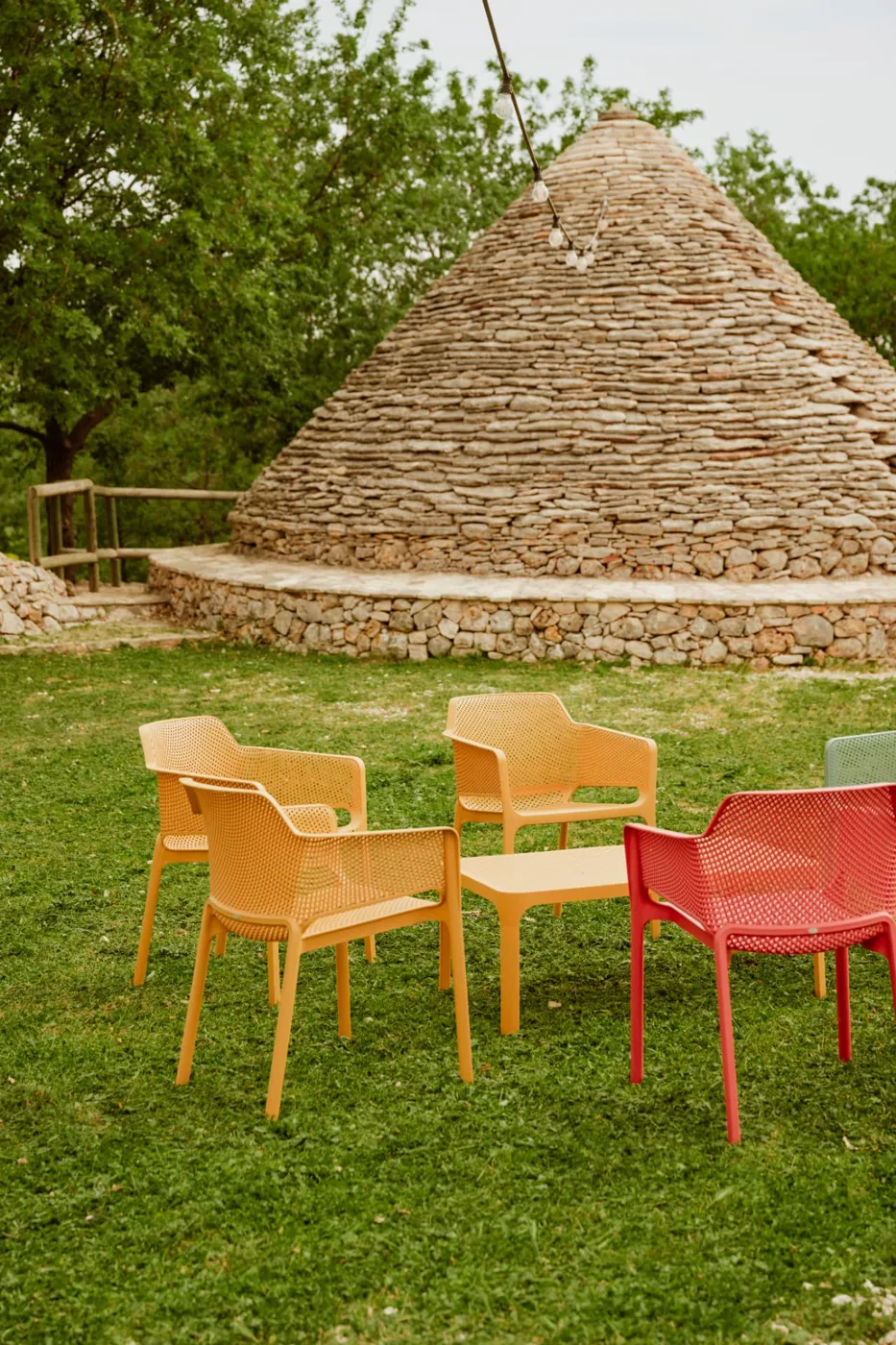 Sedute colorate sul prato davanti a un trullo in pietra a secco