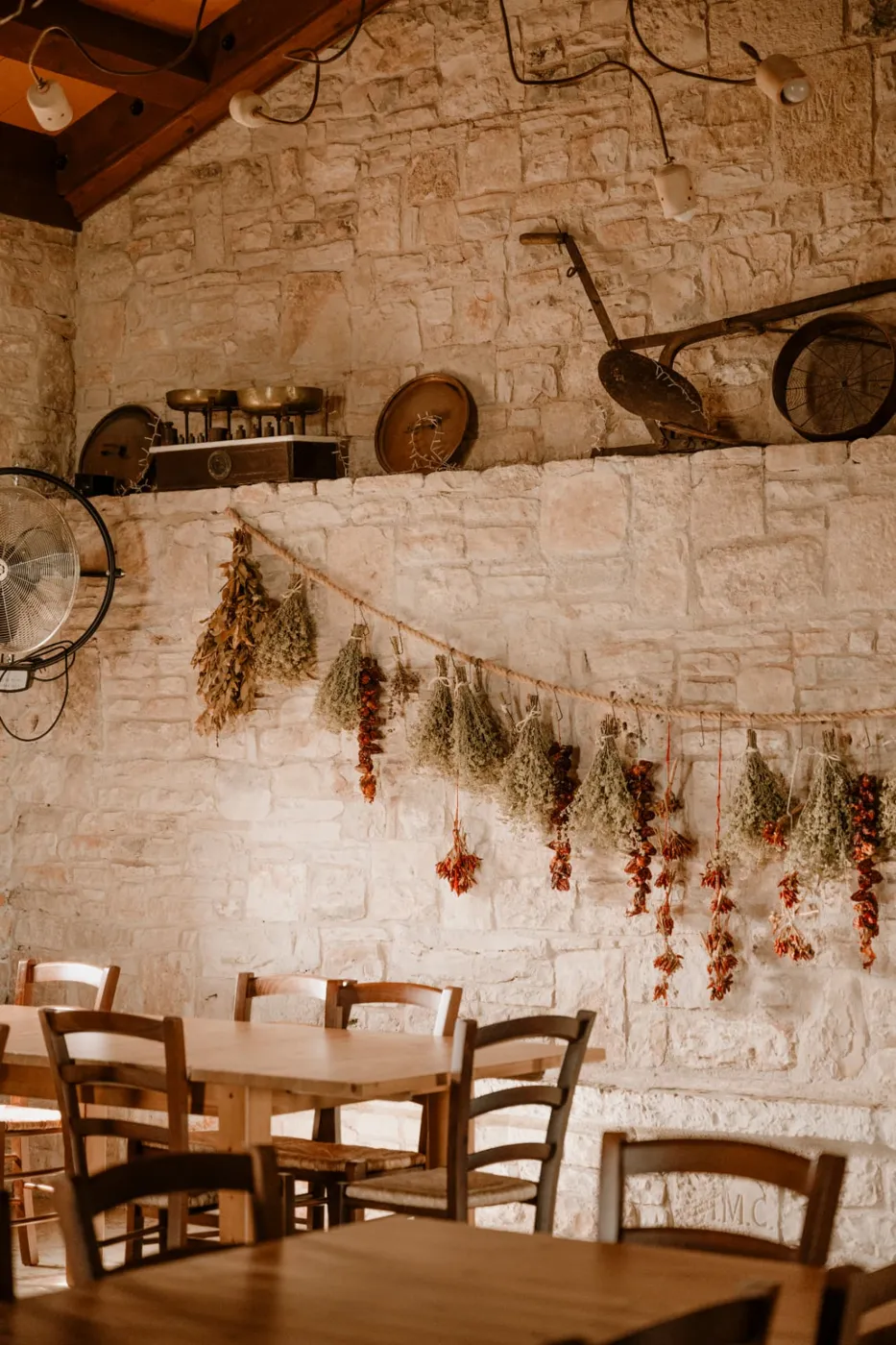 Sala interna in pietra con tavoli in legno e mazzi di erbe e peperoni appesi