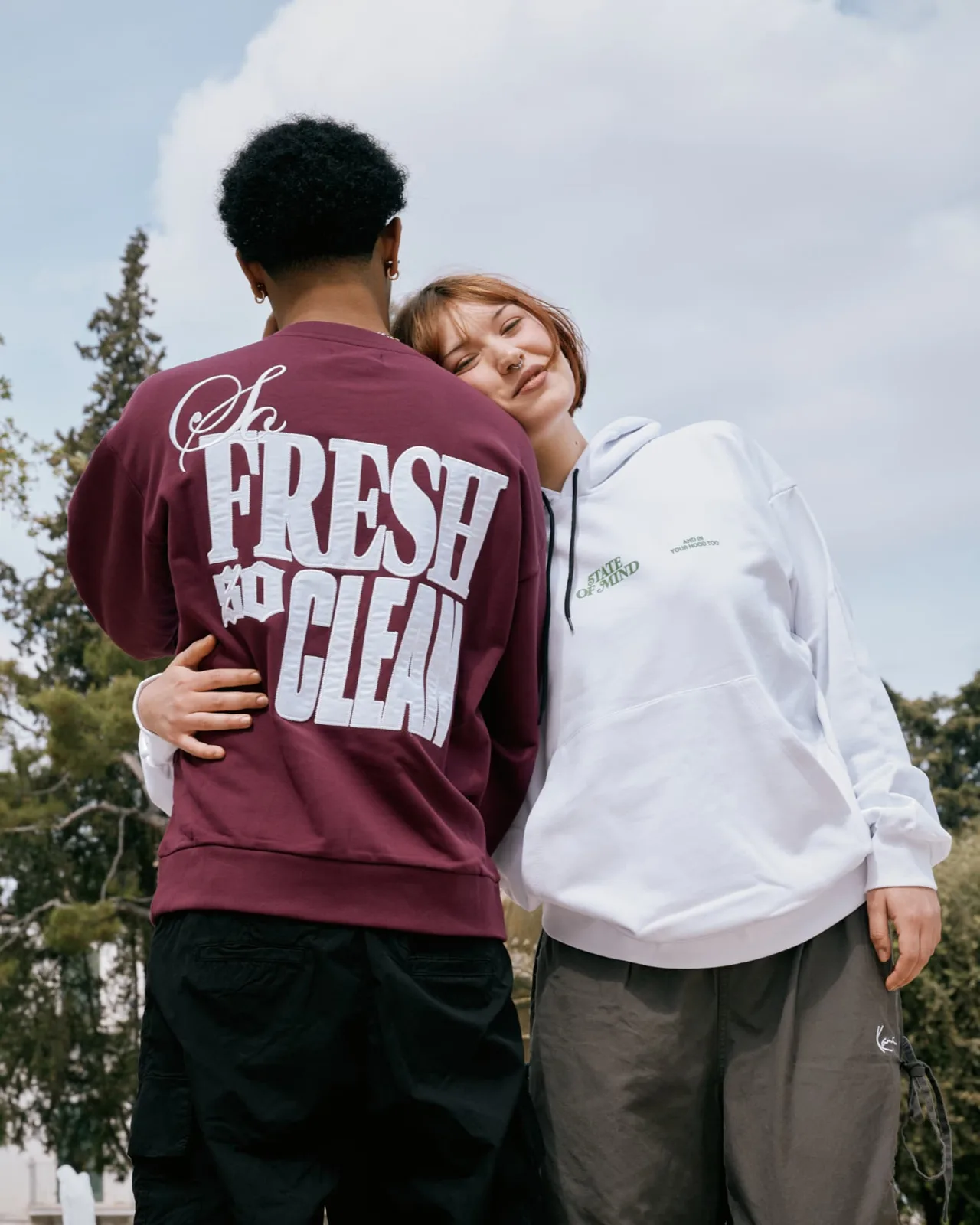 Due modelli abbracciati con felpa bordeaux e hoodie bianca