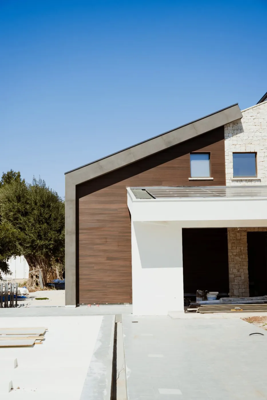 Facciata di una villa contemporanea con rivestimento in legno, pietra e cemento sotto cielo terso