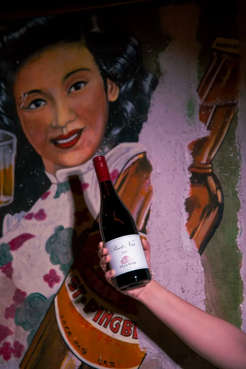 Bottiglia di vino rosso in mano davanti al murale del locale