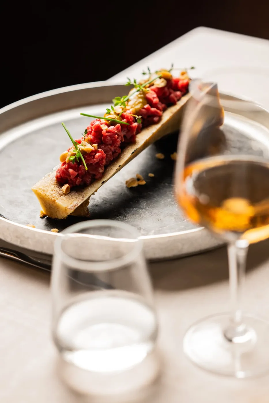 Tartare nell’osso su piatto in metallo con calice di vino
